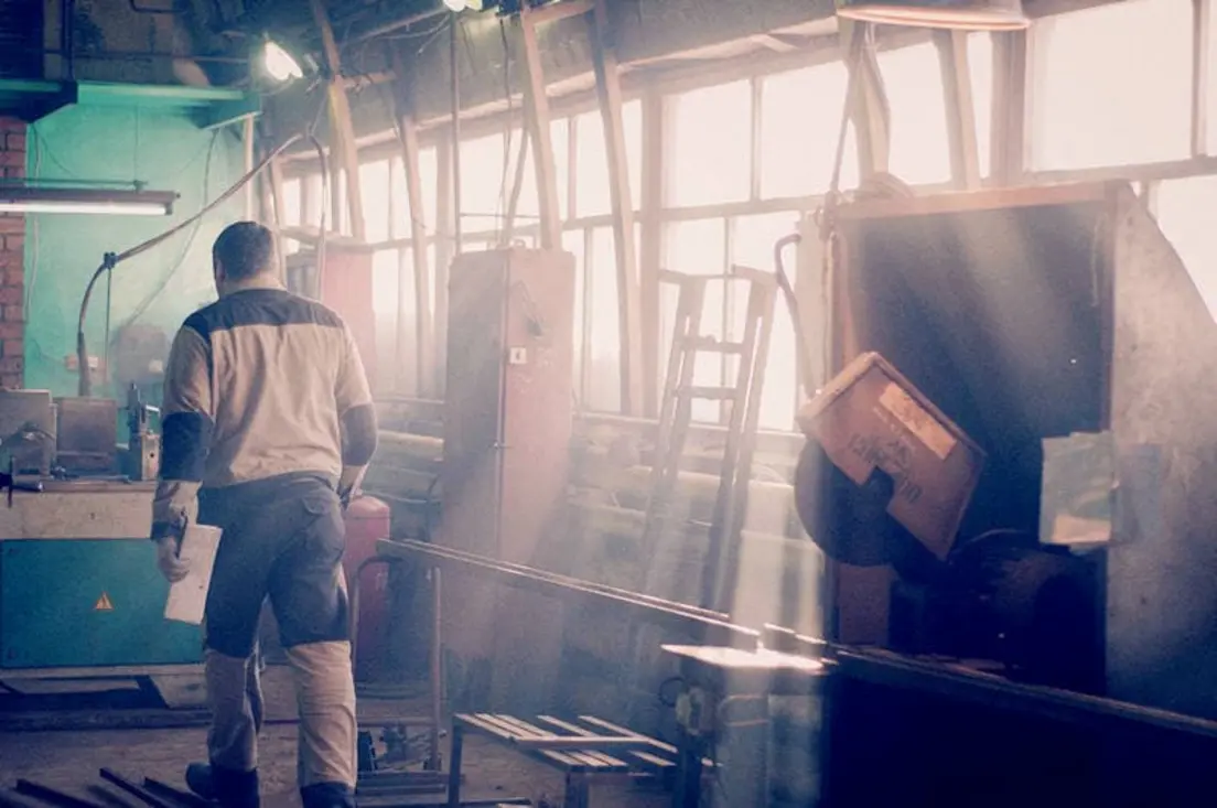 A worker walks through a well-lit industrial space with sunlight streaming through large windows.